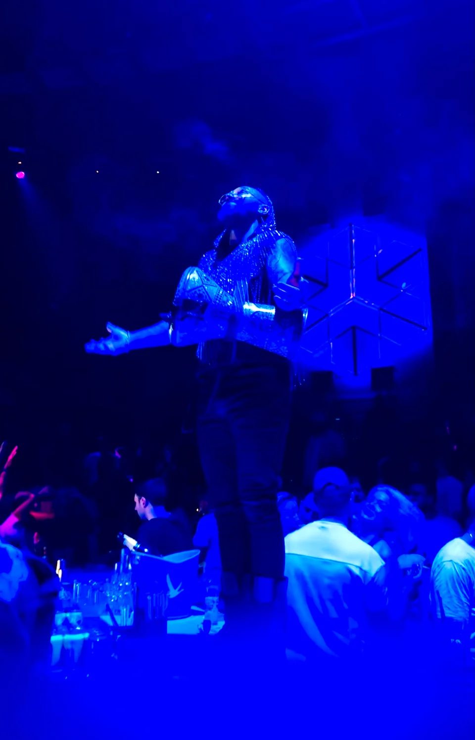 A performer standing with arms out beneath blue lights at WHITE Abu Dhabi