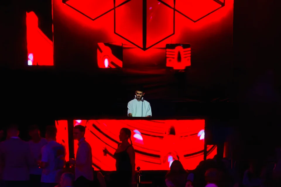 A DJ behind a booth beneath a red geometric light installation at WHITE Abu Dhabi