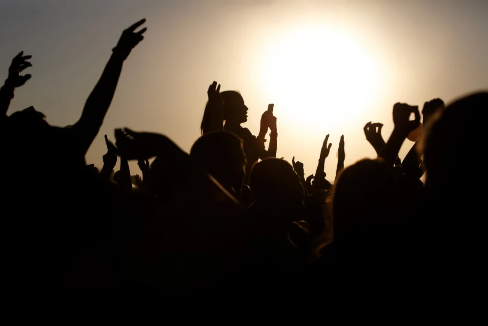 Silhouettes of festivalgoers with raised arms against the setting sun