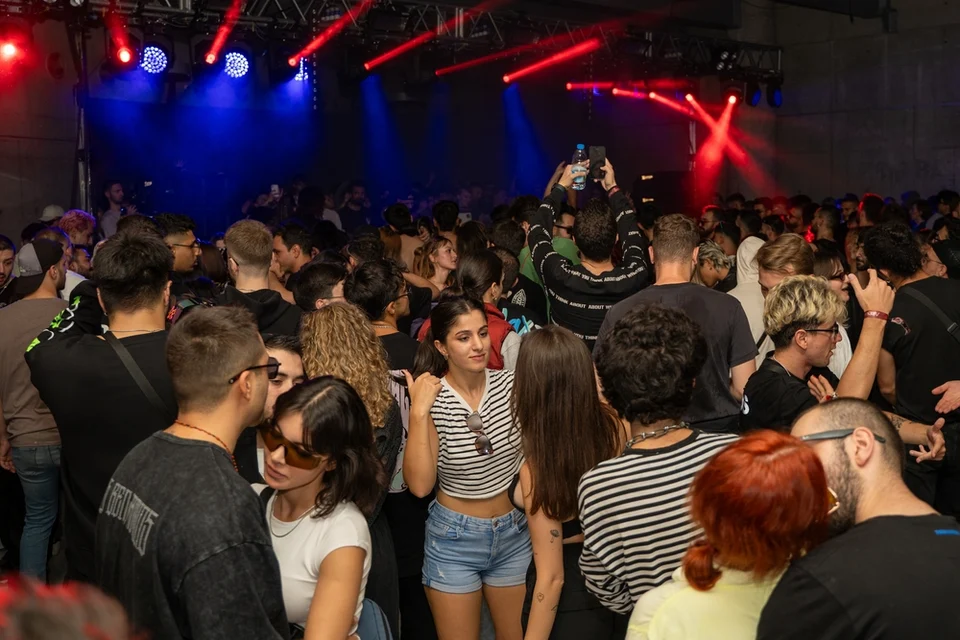 A crowd beneath red and blue lights, with a person holding a phone above their head