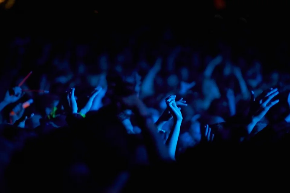 People raising their hands beneath blue stage lights