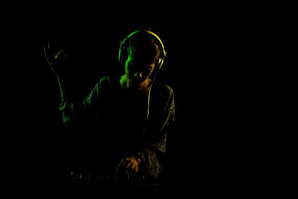 A DJ wearing headphones at a mixer under green side lighting