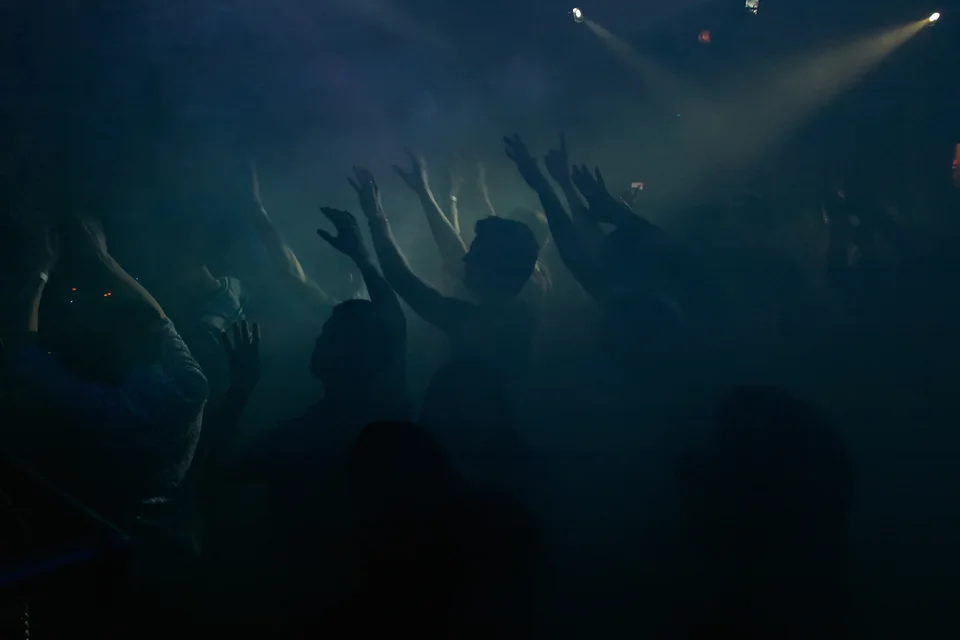 Silhouettes dancing beneath spotlights in a room filled with haze